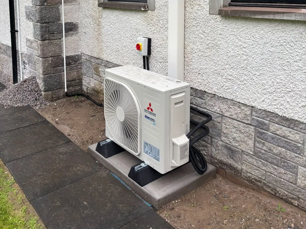 Compact Mitsubishi outdoor air conditioning unit installed neatly against a Highland bungalow, with the pipework concealed in white trunking