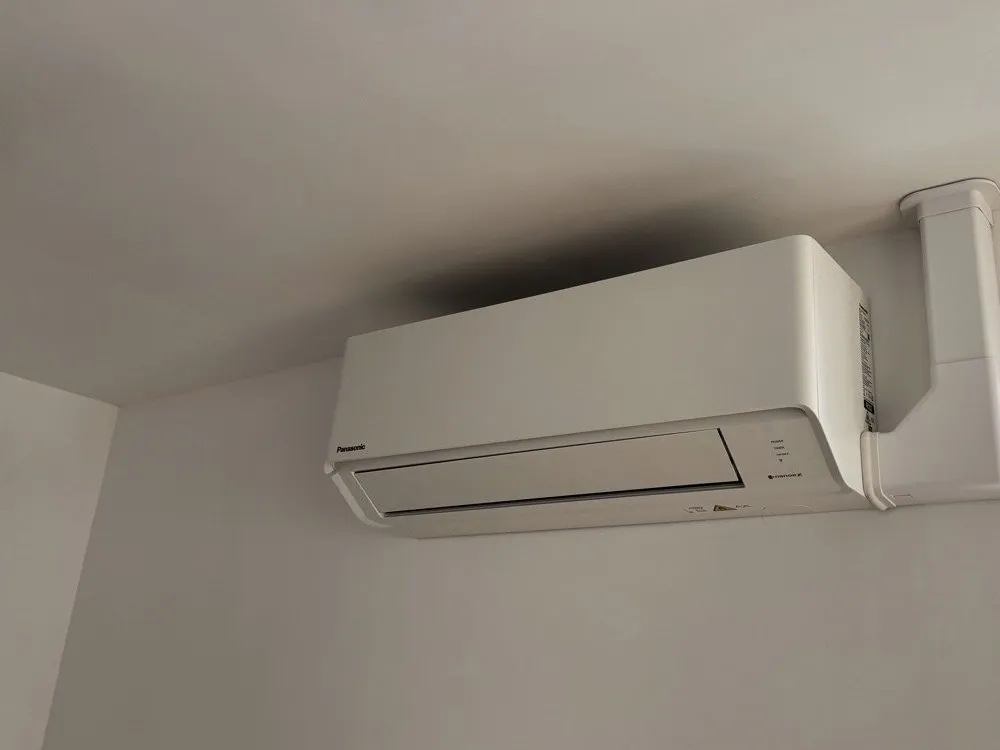White Panasonic wall-mounted air conditioning unit installed high on a bedroom wall in Auldearn