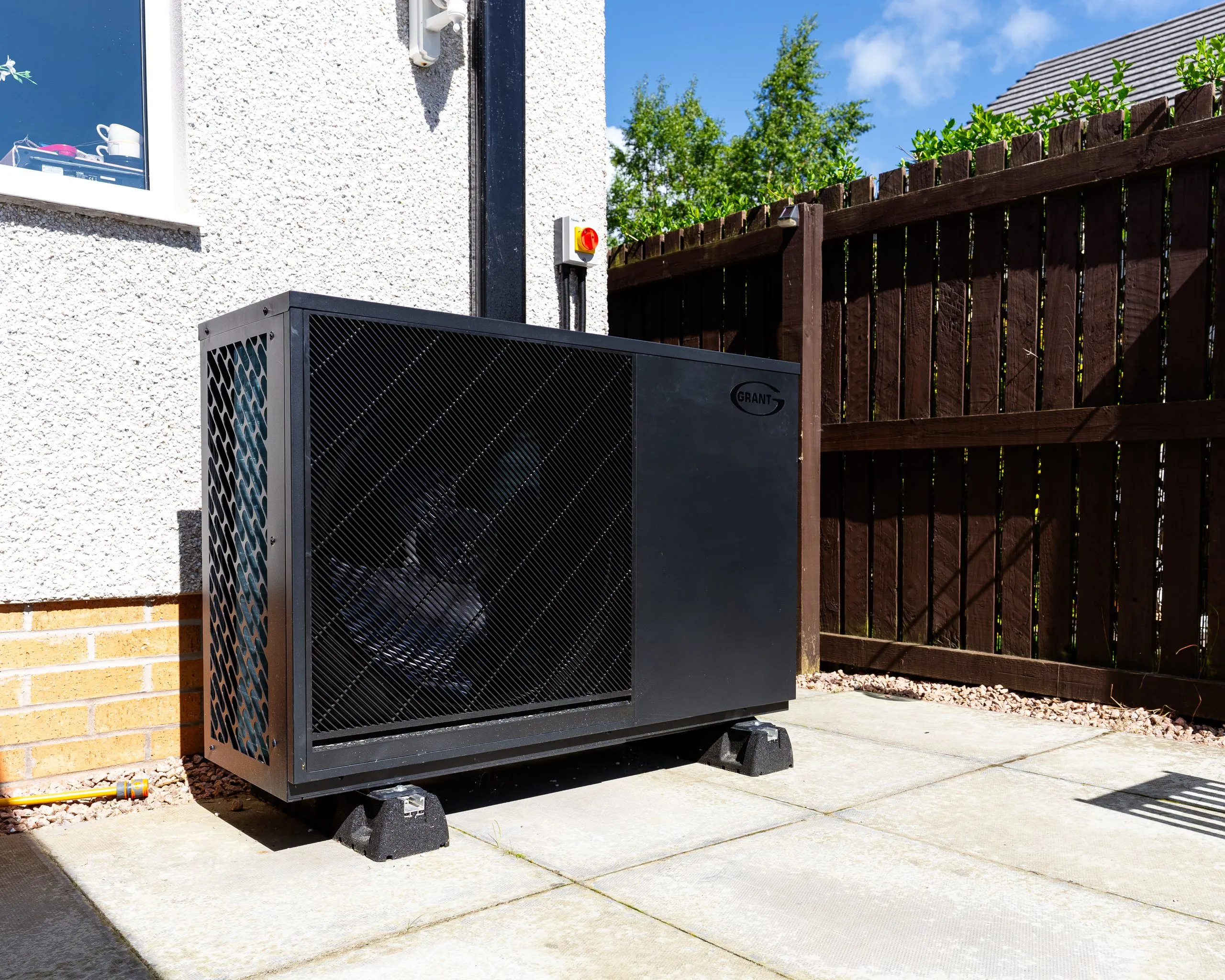Black Grant Aerona heat pump installed on rubber feet on a patio beside a Highland home
