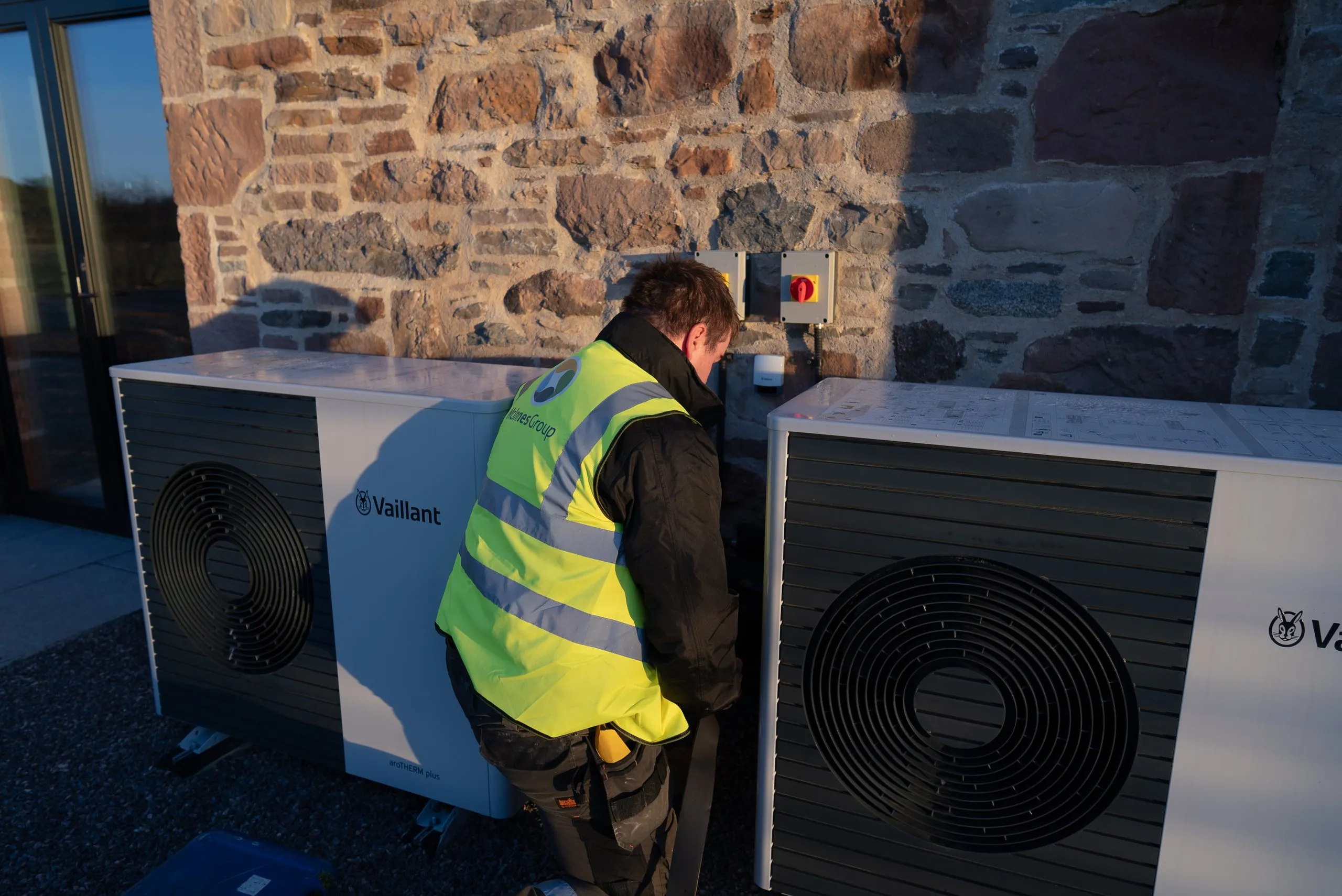 Two Vaillant air source heat pump units installed against a stone wall by a McInnes Group engineer