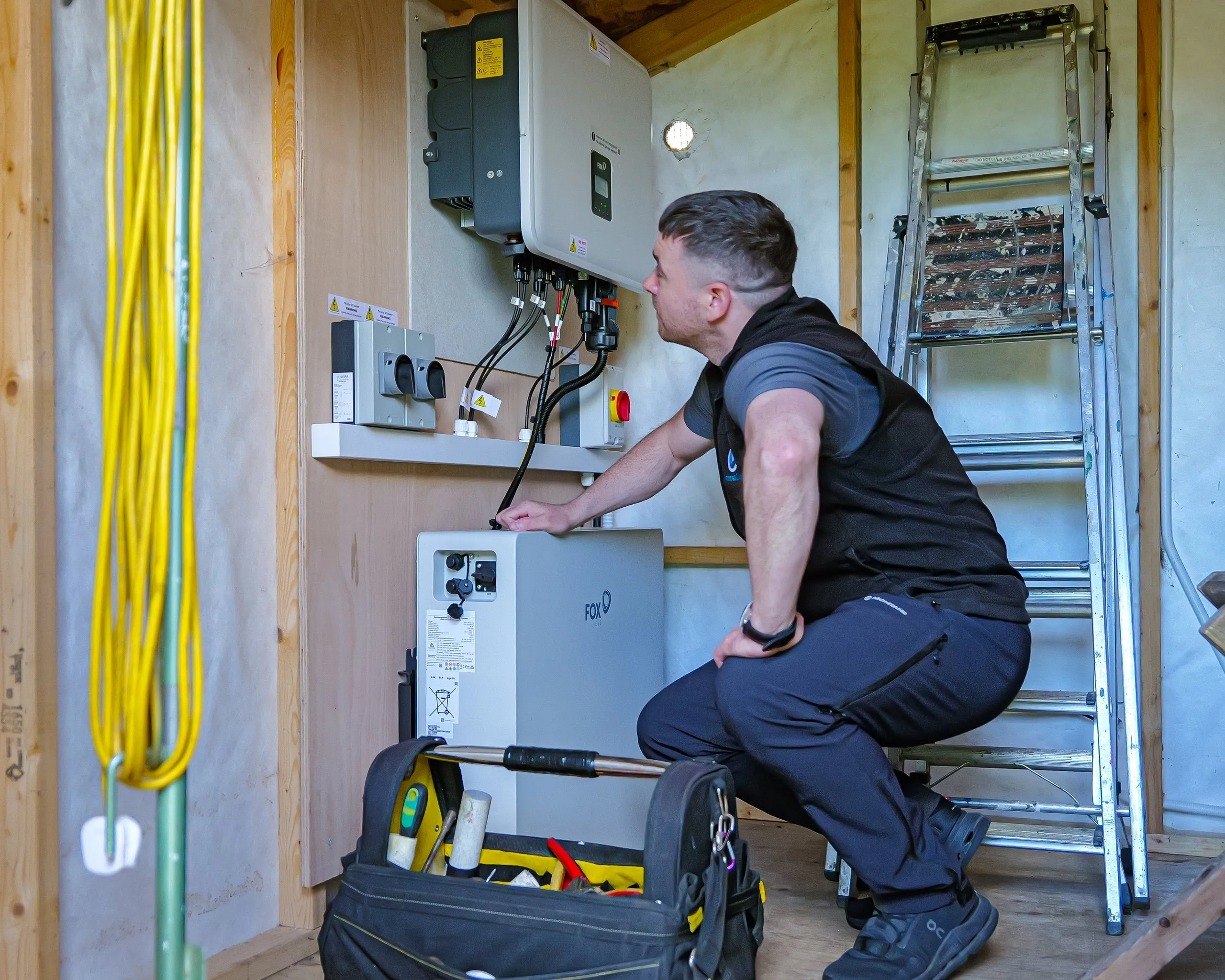A finished home battery installation in a plywood-lined loft — wall-mounted battery cabinet flanked by two inverters