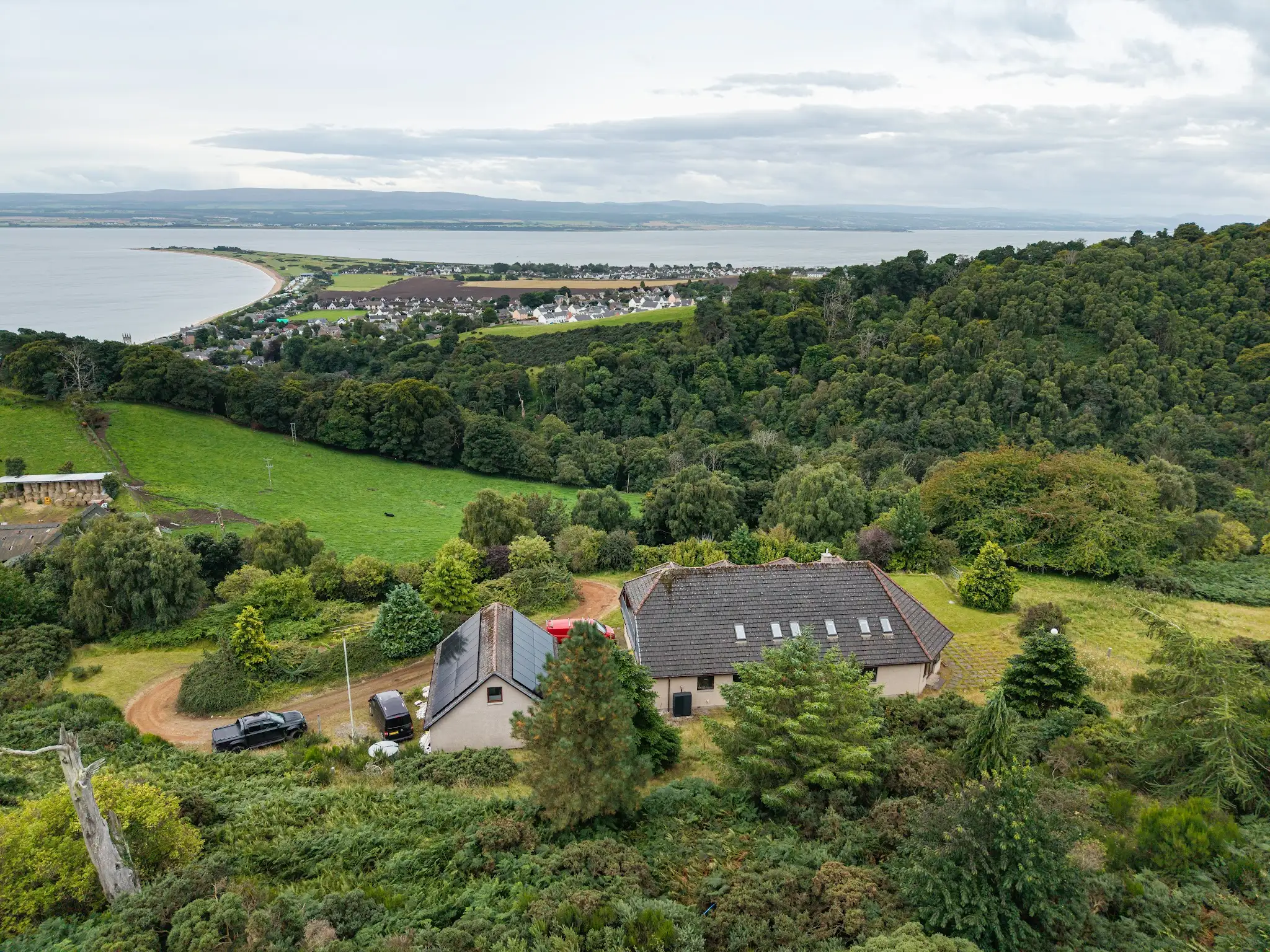 Drone view of a Scottish home with an east-west split solar array on the roof, looking out over the firth