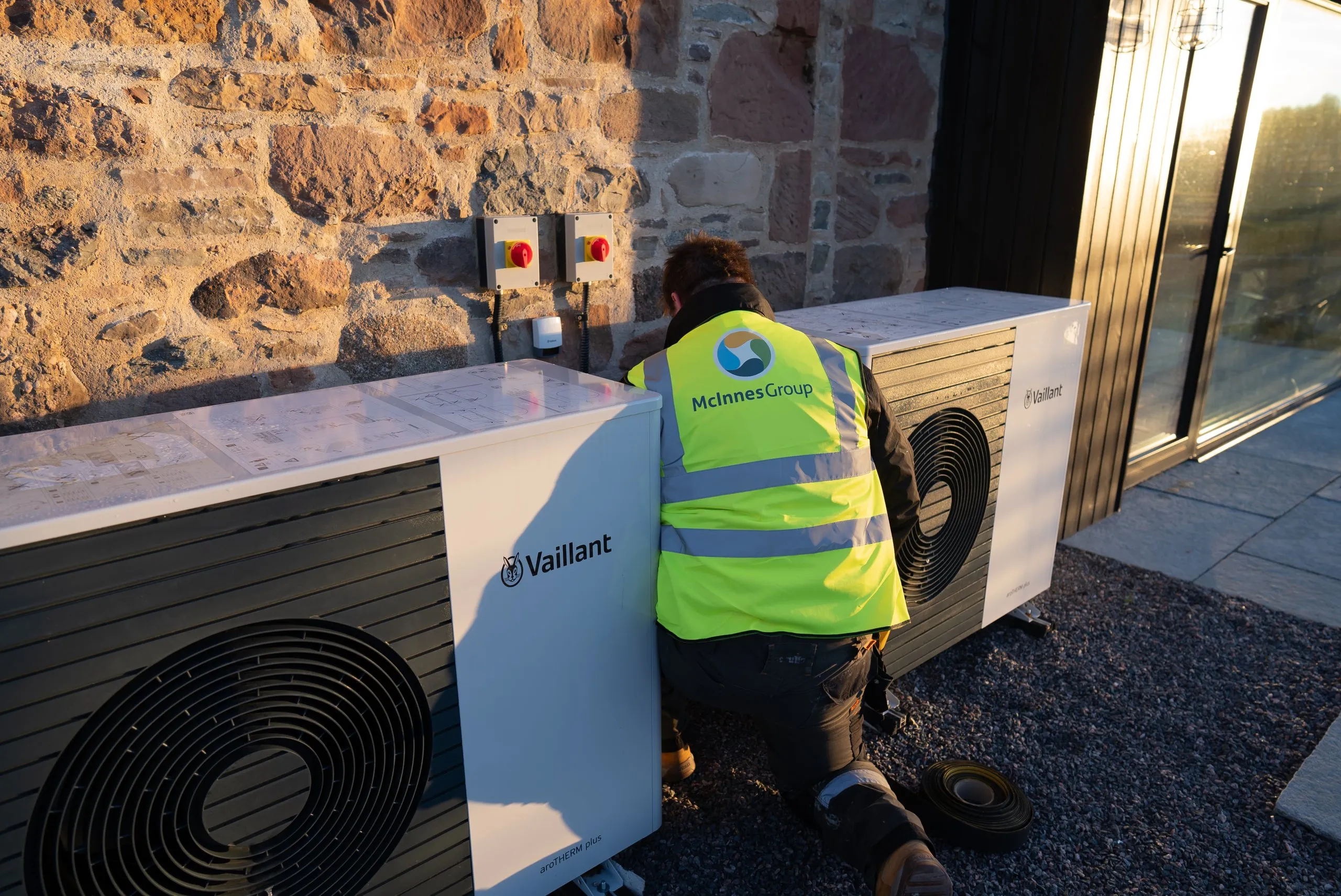 A McInnes Group engineer commissioning the two Vaillant aroTHERM plus heat pumps in cascade against the steading's stone wall