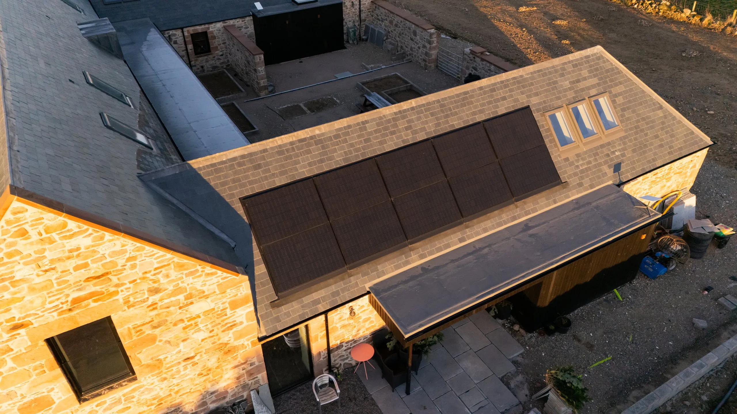 Golden-hour drone view of in-roof solar panels across the slate roof of the steading conversion near Culloden
