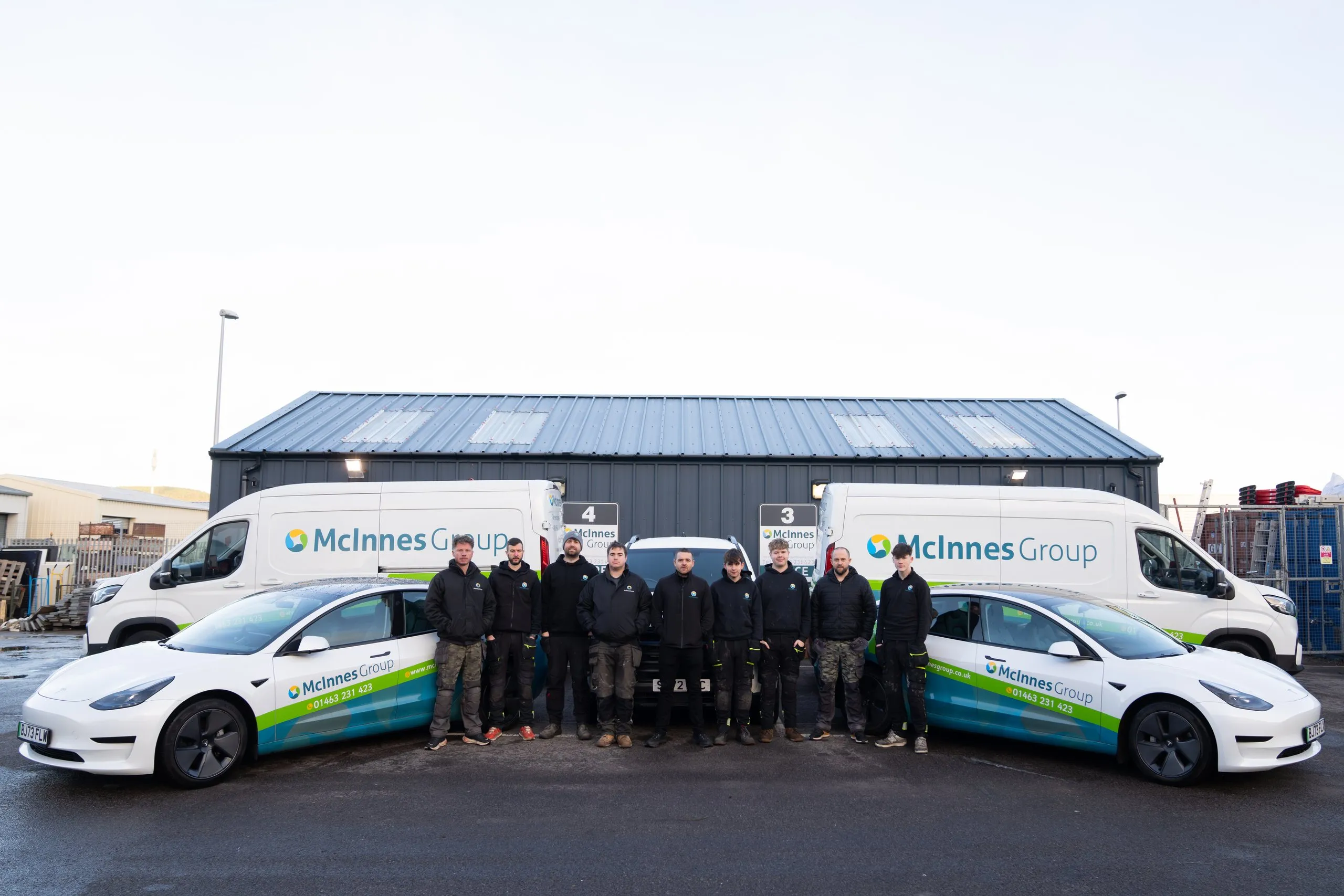 The McInnes Group engineering team lined up in front of the Inverness HQ with branded vans and Tesla Model 3s